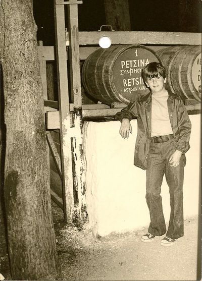 A young boy poses near a wooden barrel in a rustic setting.